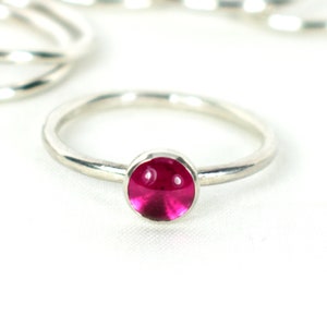 May include: A silver ring with a bright pink gemstone set in a bezel setting.