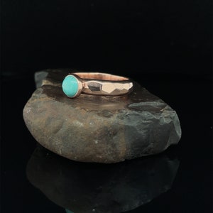 May include: A rose gold ring with a turquoise gemstone. The ring band is hammered and has a textured finish.