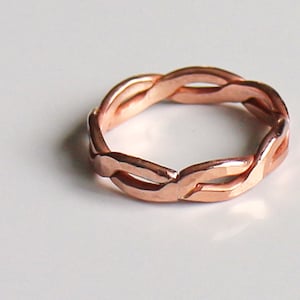 May include: A rose gold braided ring with a simple design.
