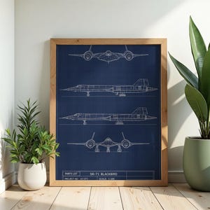 Op de afbeelding: Een ingelijste blauwdruk-kunstdruk met witte lijntekeningen van het SR-71 Blackbird-vliegtuig op een donkerblauwe achtergrond. De print toont vier aanzichten van het vliegtuig, een onderdelenlijst, projectnummer AV-071 en een schaal van 1:100.