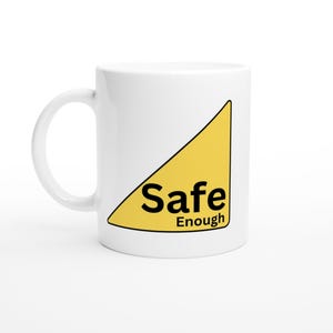 May include: A white ceramic mug featuring a yellow right-angled triangle graphic on the side. Inside the yellow triangle, the text "Safe" is printed in large black letters above the word "Enough" in smaller black letters.