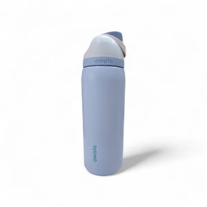 May include: A light blue Owala water bottle with a cylindrical body and a white lid featuring a carry loop. The brand name Owala is printed in dark text on the lower body and embossed on the lid collar. The bottle has a smooth matte finish.