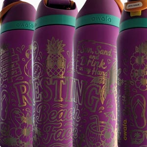 May include: Four purple Owala water bottles with teal accents and orange carry loops. Each bottle features gold-toned laser-engraved tropical designs, including pineapples, flamingos, and text such as Resting Beach Face and Sun, Sand, and Drink in my Hand.