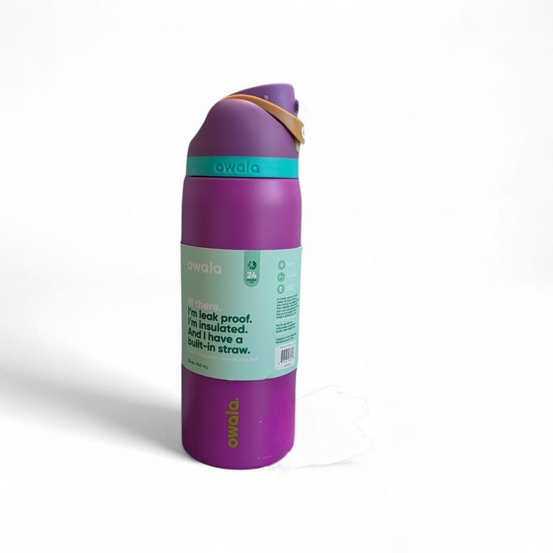 May include: A purple Owala insulated water bottle with a teal lid and a tan carry loop. The bottle features a label with the text: Hi there. I'm leak proof. I'm insulated. And I have a built-in straw. The bottle has a capacity of 24 ounces.
