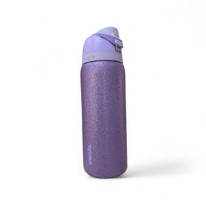 May include: A cylindrical water bottle with a glittery purple finish and a light purple lid. The bottle features the brand name Owala printed in white near the base and on the lid. The lid includes a push-button mechanism and a carry loop.