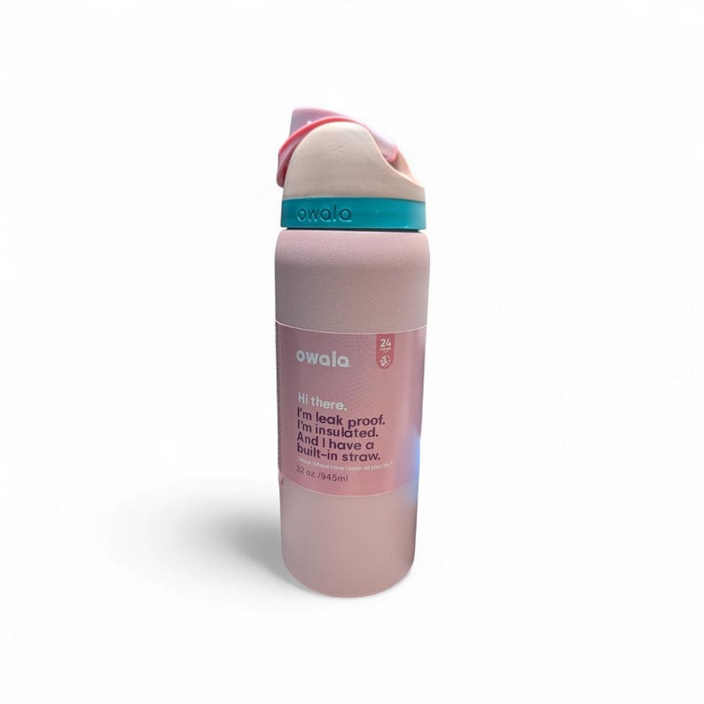 May include: A light pink insulated water bottle with a teal accent band and a pink lid. The bottle features a label with the text: Owala, Hi there. I'm leak proof. I'm insulated. And I have a built-in straw. 32 oz./945ml. The bottle has a matte finish.