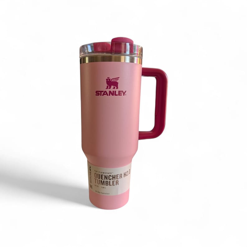 May include: A pink Stanley Quencher H2.0 Flowstate tumbler with a handle. The tumbler has a clear lid and a dark pink handle and accents. The Stanley logo is printed in dark pink. The tumbler has a capacity of 40 oz.