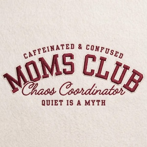 May include: Cream-colored textile with embroidered text in burgundy. The text reads "CAFFEINATED & CONFUSED" above "MOMS CLUB" and "Chaos Coordinator". Below is the phrase "QUIET IS A MYTH".