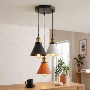 May include: A three-light pendant fixture featuring a circular black ceiling canopy with three adjustable black cords. Each cord supports a conical metal shade in matte black, white, and terracotta, accented with brass-toned hardware and bulbs.