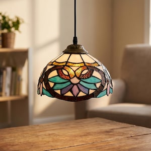 Könnte beinhalten: Eine Hängelampe mit einem Buntglasschirm. Der Schirm hat ein Blumenmuster mit blauen, violetten und braunen Akzenten. Die Lampe hängt an einem schwarzen Kabel über einem Holztisch. Eine dekorative Beleuchtung.
