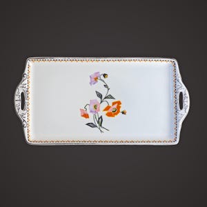 May include: White rectangular serving tray with a floral design. The tray has a border of orange and brown dots, and handles at each end. The floral design features orange, pink, and purple flowers with green stems.
