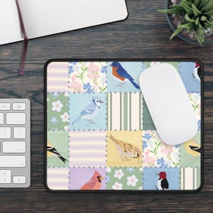 May include: A rectangular mousepad with a patchwork design featuring various colorful birds. The birds are set against a backdrop of floral and striped patterns in pastel colors. A white computer mouse rests on the pad.