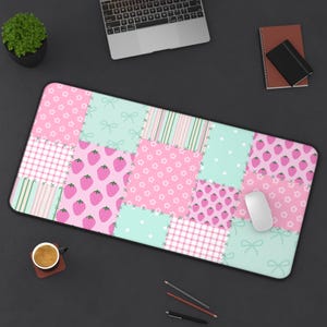 Peut inclure: Un grand tapis de bureau rectangulaire avec un motif patchwork rose, vert menthe et blanc. Le motif comprend des fraises, des nœuds, des pois et des rayures. Une souris d'ordinateur blanche est posée sur le tapis.