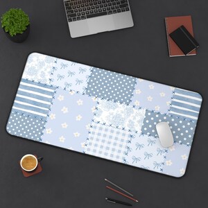 Peut inclure: Tapis de bureau rectangulaire avec un motif patchwork bleu et blanc. Le motif comprend des pois, des rayures, des nœuds et des éléments floraux. Une souris blanche est posée sur le tapis, avec un ordinateur portable et des fournitures de bureau.