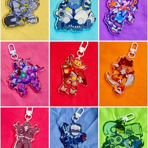 Puede incluir: Una colecci&oacute;n de nueve llaveros de acr&iacute;lico transparente con personajes ilustrados coloridos en varias poses, cada uno unido a un cierre de mosquet&oacute;n de pl&aacute;stico blanco. Los dise&ntilde;os incluyen figuras con armadura y entidades rob&oacute;ticas.