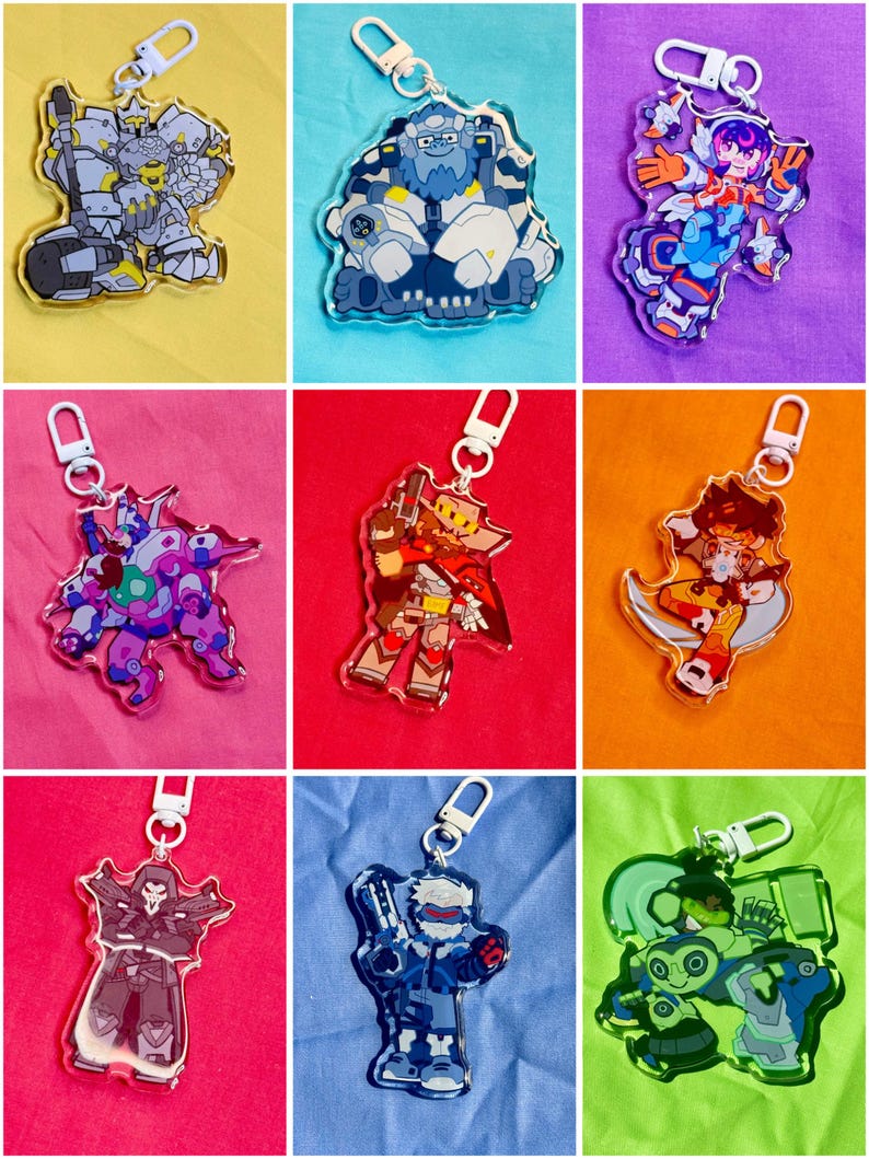 Puede incluir: Una colecci&oacute;n de nueve llaveros de acr&iacute;lico transparente con personajes ilustrados coloridos en varias poses, cada uno unido a un cierre de mosquet&oacute;n de pl&aacute;stico blanco. Los dise&ntilde;os incluyen figuras con armadura y entidades rob&oacute;ticas.