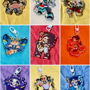 Puede incluir: Una colecci&oacute;n de nueve llaveros de acr&iacute;lico con diversos personajes ilustrados en colores vibrantes, cada uno unido a un cierre de mosquet&oacute;n de pl&aacute;stico claro. Los dise&ntilde;os incluyen varias figuras en poses din&aacute;micas, mostrando l&iacute;neas detalladas y paletas audaces.