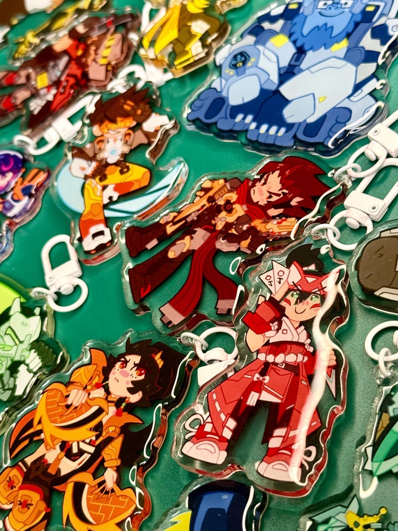 Puede incluir: Una colecci&oacute;n de llaveros de acr&iacute;lico transparente con coloridas ilustraciones de personajes estilo anime. Cada dije incluye un broche de langosta de pl&aacute;stico blanco y muestra figuras distintas en poses din&aacute;micas con paletas de colores vibrantes.