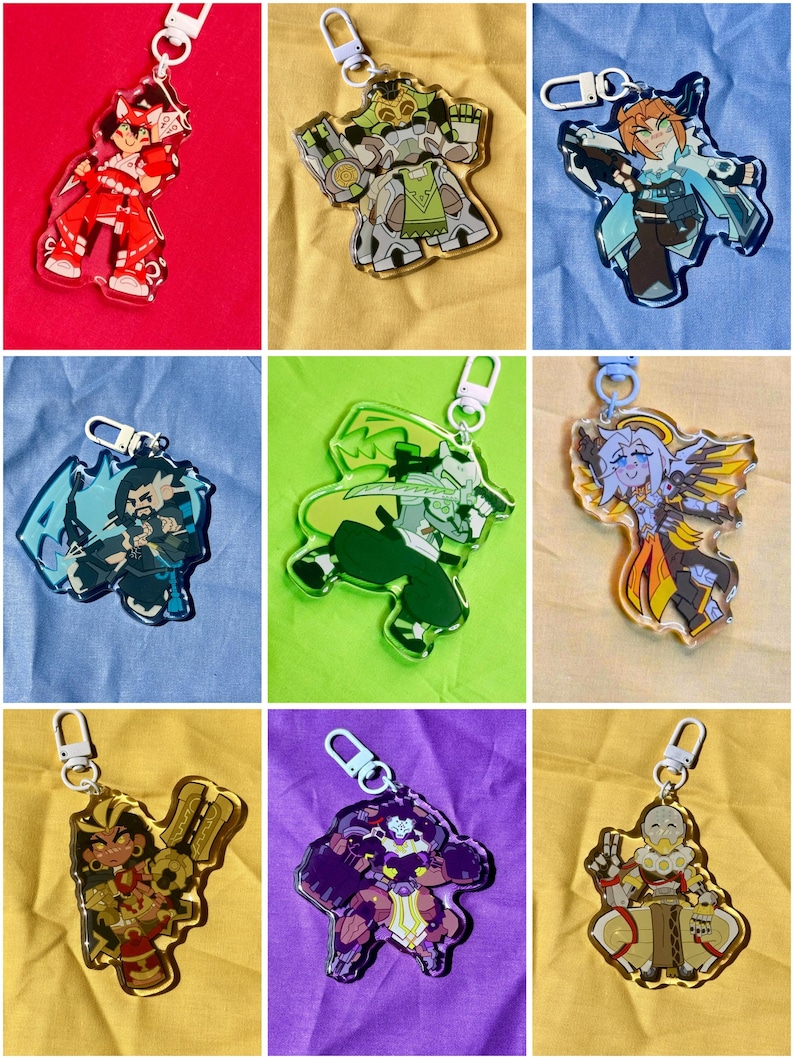 Puede incluir: Una colecci&oacute;n de nueve llaveros de acr&iacute;lico con diversos personajes ilustrados en varias poses y esquemas de color, cada uno unido a un cierre giratorio de pl&aacute;stico blanco o azul claro, mostrando dise&ntilde;os gr&aacute;ficos detallados y definidos.