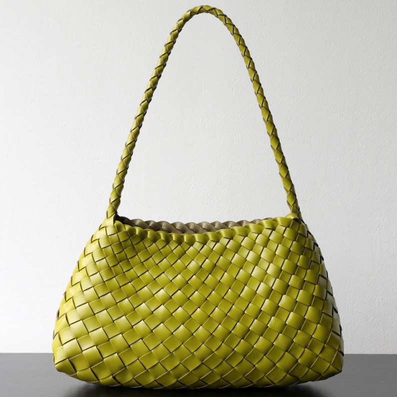 May include: A lime green woven handbag with a braided handle. The bag has a rectangular shape with a woven pattern. The handle is a single, long braid. The bag is sitting on a dark surface against a white background.