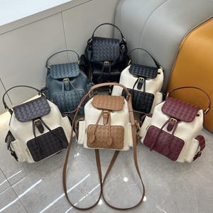 Puede incluir: Una colección de seis mochilas pequeñas con solapa y bolsillo frontal de aspecto trenzado, asa superior, correas ajustables y cierre de hebilla. Las mochilas están disponibles en colores negro, azul, crema, marrón y burdeos.