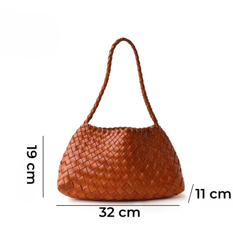 May include: A brown woven handbag with a braided handle. The bag is 32 cm long, 19 cm high, and 11 cm wide. The bag has a rounded shape and is made of a woven material.