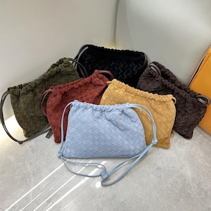 May include: A collection of woven drawstring bags in various colors, including light blue, black, brown, yellow, red, and olive green. Each bag features a woven pattern and a drawstring closure. The bags are displayed on a light-colored surface.