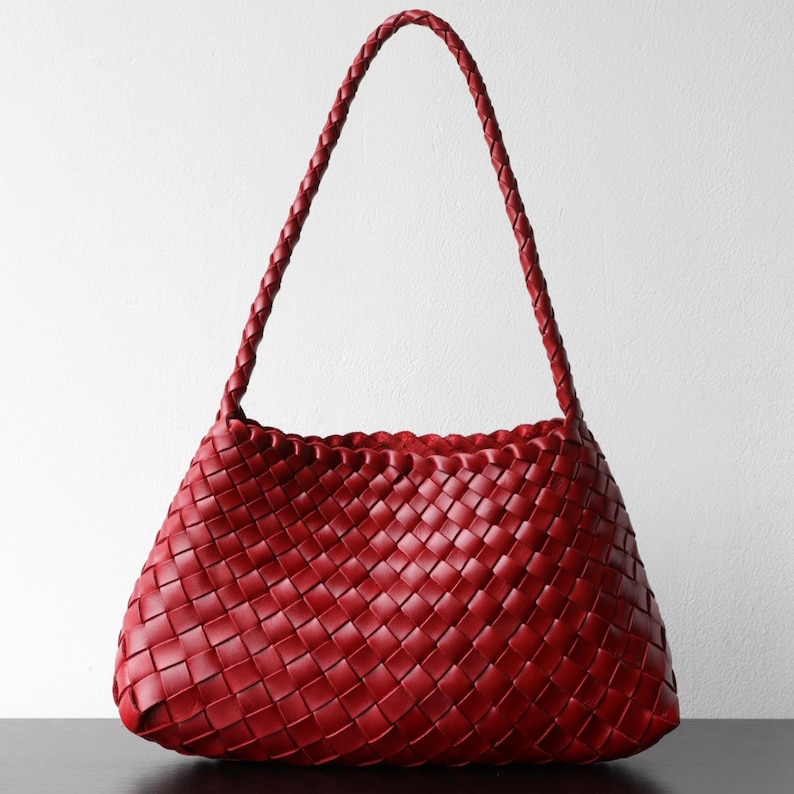 May include: A red woven leather handbag with a plaited handle. The bag has a trapezoid shape with a scalloped top edge. The woven pattern is visible across the entire surface of the bag.