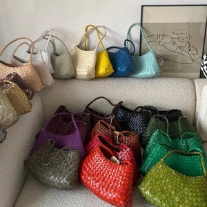 Peut inclure: Plusieurs sacs à main tressés de différentes couleurs, dont beige, jaune, bleu et vert. Les sacs ont un aspect texturé et sont disposés sur une surface blanche. Certains sacs ont des anses, pour un style décontracté et élégant.