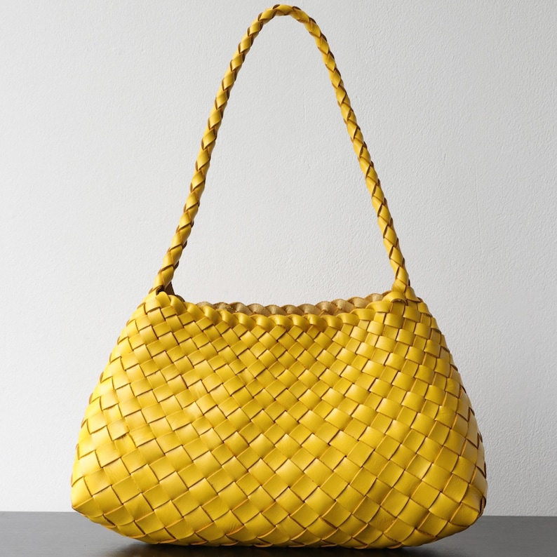 May include: A bright yellow woven handbag with a braided handle. The bag's body has a rectangular shape with rounded edges and a woven pattern. The handle is a single, long braid.