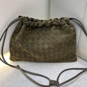 Puede incluir: Bolso con cord&oacute;n de ante verde oliva con un patr&oacute;n tejido. El bolso tiene una correa larga y delgada y un cierre de cord&oacute;n. El bolso es de color neutro y es adecuado para el uso diario.