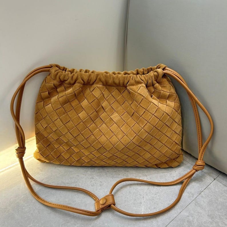 Puede incluir: Bolso de mano de ante color mostaza con dise&ntilde;o tejido. El bolso cuenta con una correa larga y ajustable y un cierre de bot&oacute;n. La textura y el color del bolso le dan un aspecto suave y lujoso. Un accesorio elegante para el uso diario.