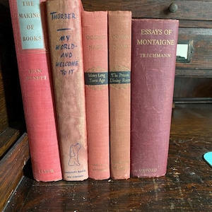 May include: A collection of vintage books with titles including "The Making of Books," "My World and Welcome to It," and "Essays of Montaigne." The books are in various shades of red and pink, with text in black and blue.