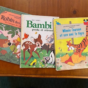 May include: Three vintage Walt Disney storybooks: "Robin des et l'attaque du can", "Bambi perdu et retrouv", and "Winnie l'ourson et son ami le tigre". The books feature colorful illustrations of the characters on their covers.