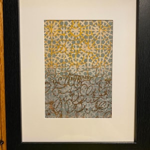 Puede incluir: Impresión artística abstracta enmarcada. La obra presenta un patrón geométrico en amarillo y blanco sobre un fondo azul grisáceo. La sección inferior tiene marcas marrones en forma de escritura arremolinada. La impresión está enmarcada con un borde blanco.