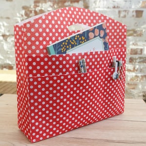 May include: Red fabric organizer with white polka dots. The organizer has three pockets and is filled with pens and a notebook.