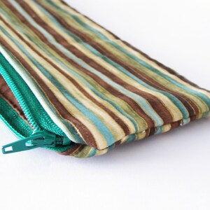 Puede incluir: Una bolsa con cremallera de rayas marrones y azul verdoso con un tirador de cremallera verde.