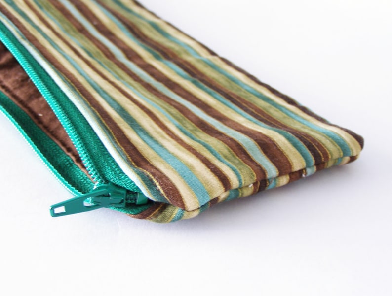 Puede incluir: Una bolsa con cremallera de rayas marrones y azul verdoso con un tirador de cremallera verde.