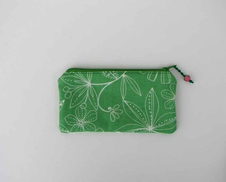 May include: A green zippered pouch with a white floral pattern. The pouch has a green zipper and a pink bead on the zipper pull.