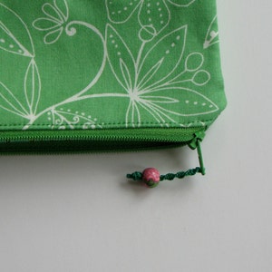 May include: A green zippered pouch with a white floral pattern and a pink bead zipper pull.