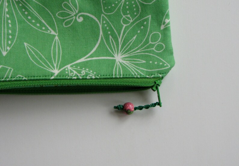 May include: A green zippered pouch with a white floral pattern and a pink bead zipper pull.