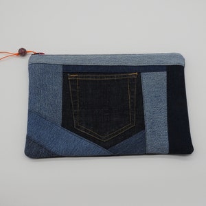 May include: A blue denim clutch purse with a patchwork design. The purse has a zipper closure and a large pocket on the front.