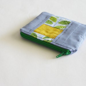 May include: A small, quilted zipper pouch with a green zipper. The pouch is made of a light blue fabric with a yellow and green patterned fabric panel.