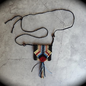 May include: A black cord necklace with a small, colorful, woven pouch with a tassel. The pouch has a geometric pattern in red, yellow, blue, and black.