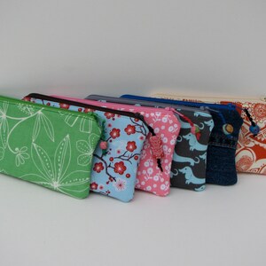 May include: A set of eight colorful zippered pouches with various patterns, including floral, geometric, and animal prints. Each pouch has a decorative bead attached to the zipper pull.
