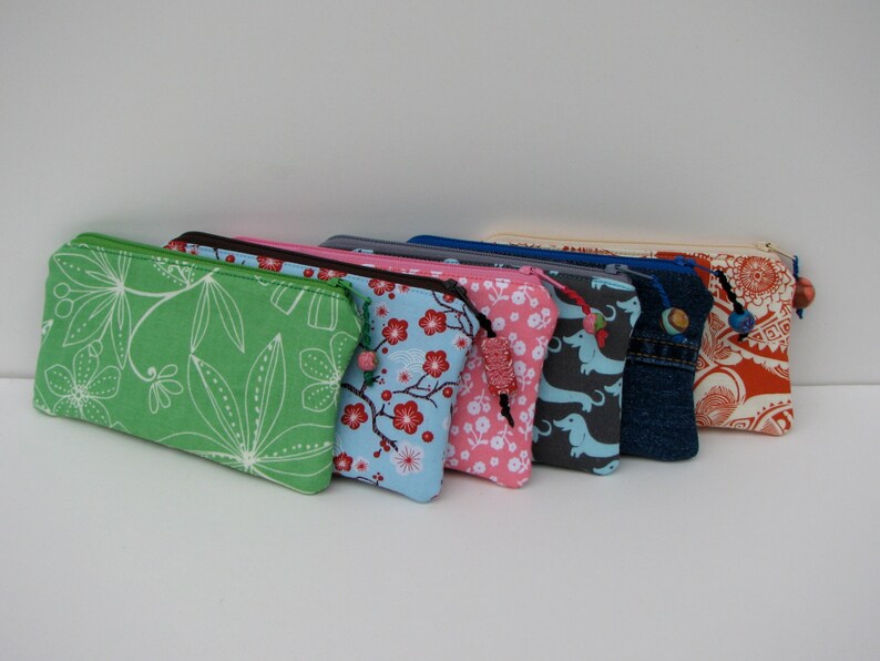 May include: A set of eight colorful zippered pouches with various patterns, including floral, geometric, and animal prints. Each pouch has a decorative bead attached to the zipper pull.