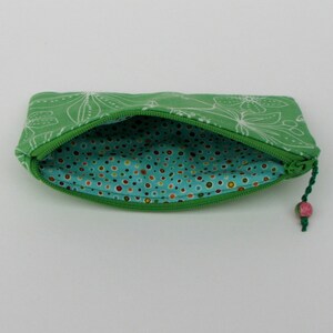 May include: A green zippered pouch with a white floral pattern on the outside and a turquoise polka dot lining on the inside. The pouch has a pink and green tassel.