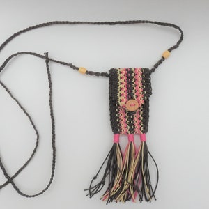 May include: A macrame phone bag with a long strap. The bag is dark brown with pink and beige stripes and a wooden button closure. The bottom features tassels in matching colours. The strap has wooden beads.