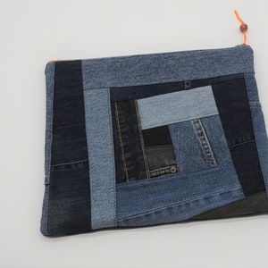 May include: A blue denim patchwork clutch bag with a zipper closure and a small orange pull tab.