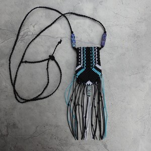Peut inclure: Un collier en macramé noir et blanc avec des perles bleues et blanches. Le collier a une frange de fils noirs, blancs et bleus.